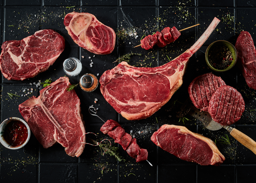 Variety of raw steaks and spices arranged on a dark surface.