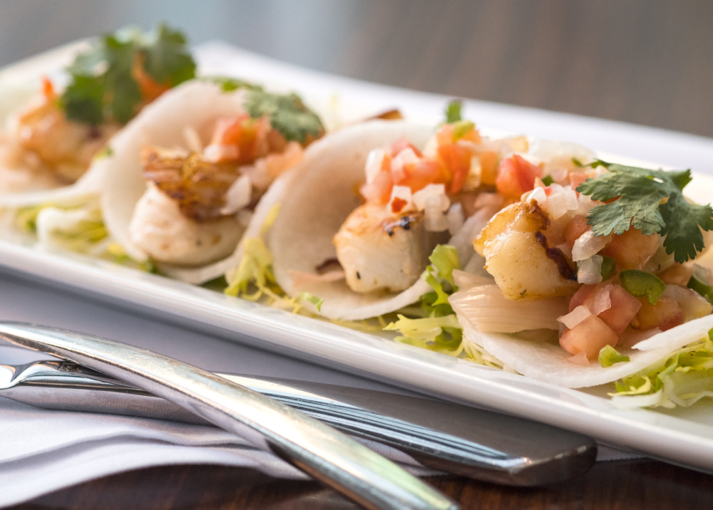 Three tacos filled with fish and fresh salsa on a white plate.